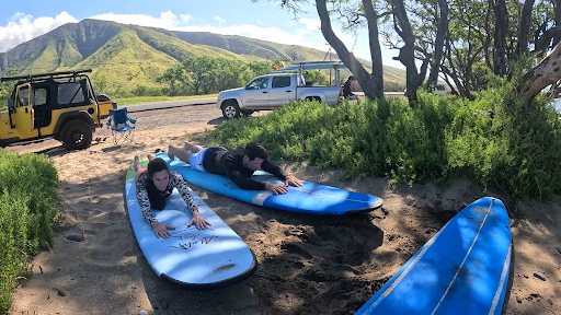 Beginner surf lesson on Maui — students practicing on surfboards on the beach with Maui mountains in the background